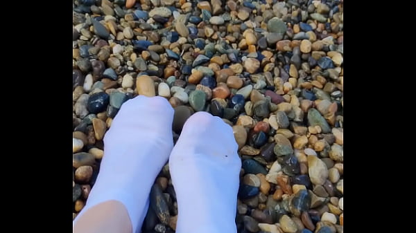 Playing with my feet in white socks with pebbles on the beach